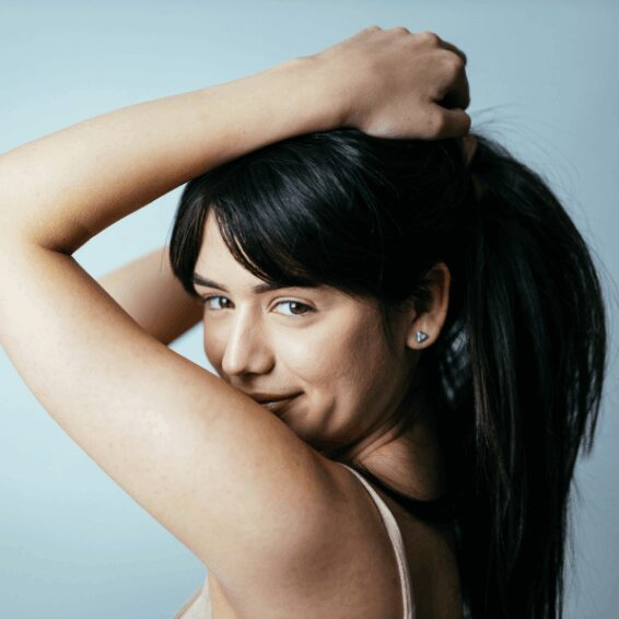 Young woman smiling with hand in her hair against a light blue background.