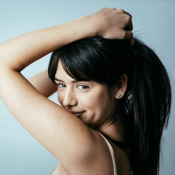 Young woman smiling with hand in her hair against a light blue background.