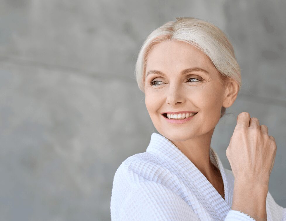 Smiling mature woman with blonde hair in a cozy white robe.