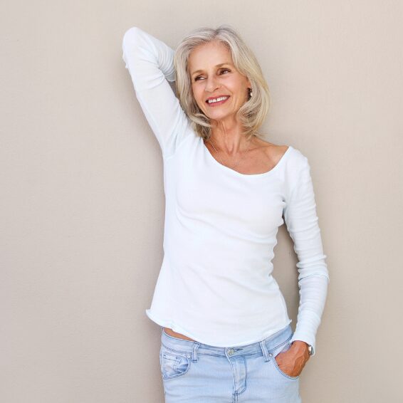 Smiling older woman posing confidently in casual white top and jeans.