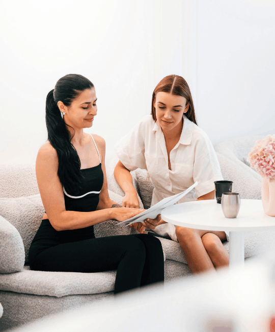 Two women discussing documents on a couch in a professional setting.