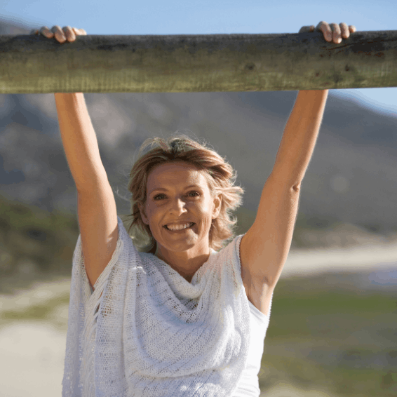 A smiling woman hanging from a wooden bar outdoors.