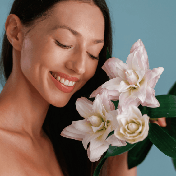A woman smiling gently while holding white lilies and greenery.
