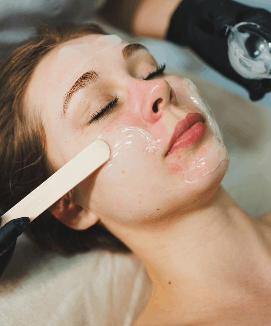Woman receiving facial treatment with a cream mask applied.