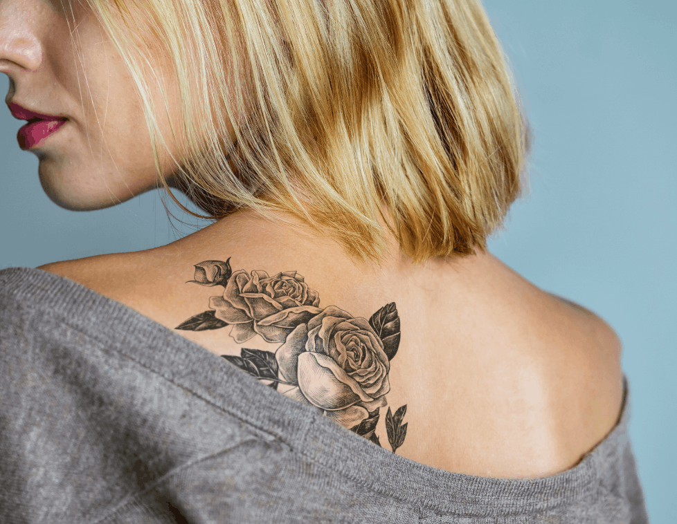 Black and grey floral tattoo on a woman's upper back with short blonde hair.