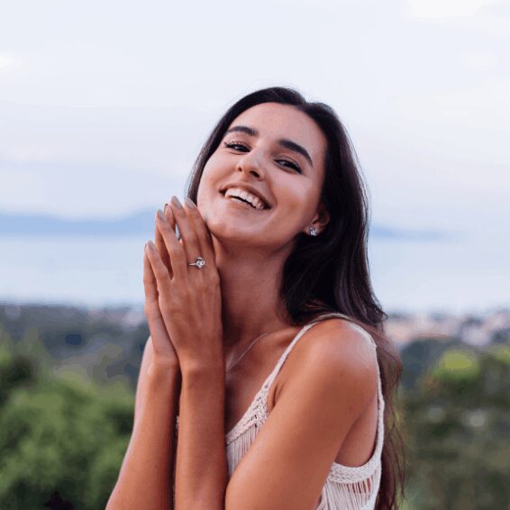 A smiling woman outdoors with hands clasped near her face.