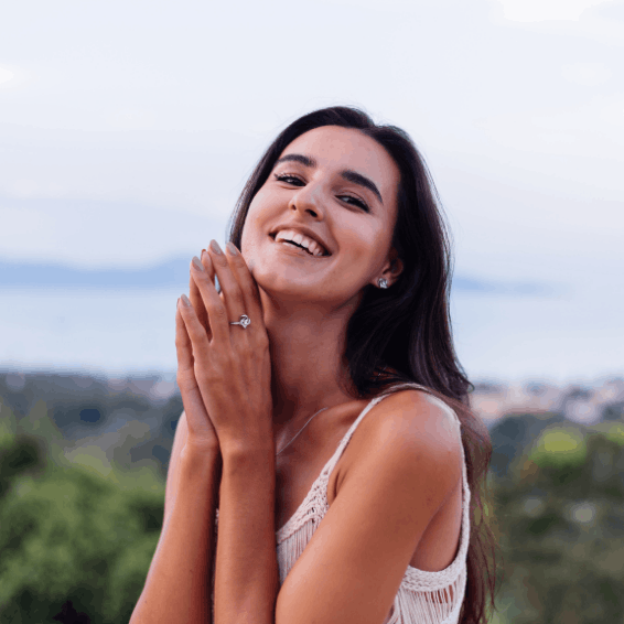 A smiling woman outdoors with hands clasped near her face.