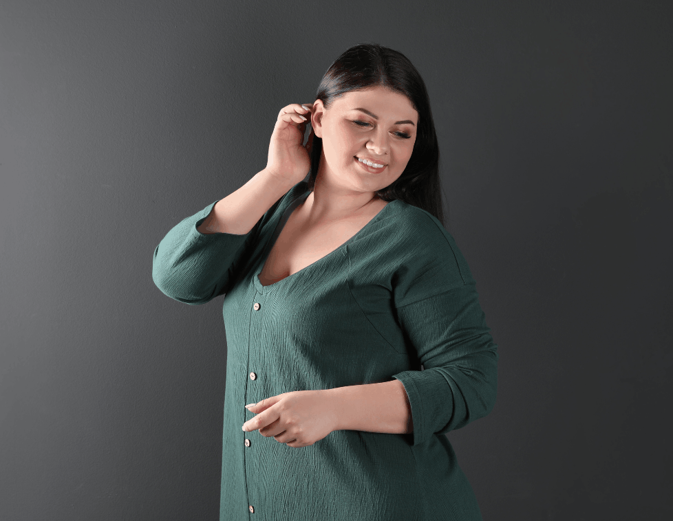 A woman in a green dress smiling and posing against a gray background.