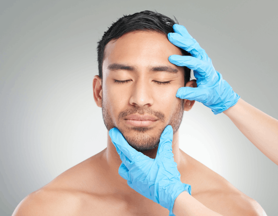 A man with closed eyes being examined by gloved hands.
