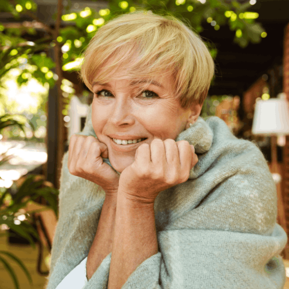 Smiling woman wrapped in a cozy blanket outdoors.