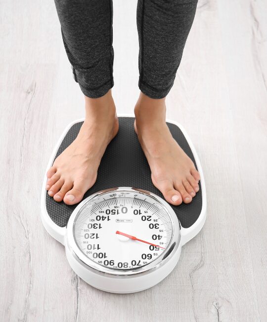 Bare feet standing on a mechanical bathroom scale on a wooden floor.