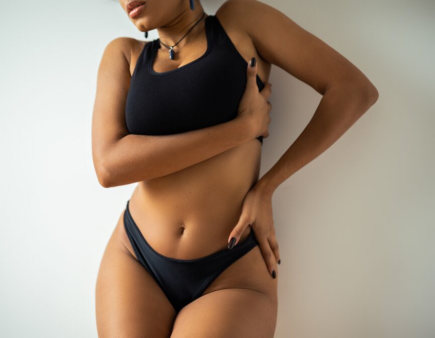 Woman in black lingerie posing against a plain wall.