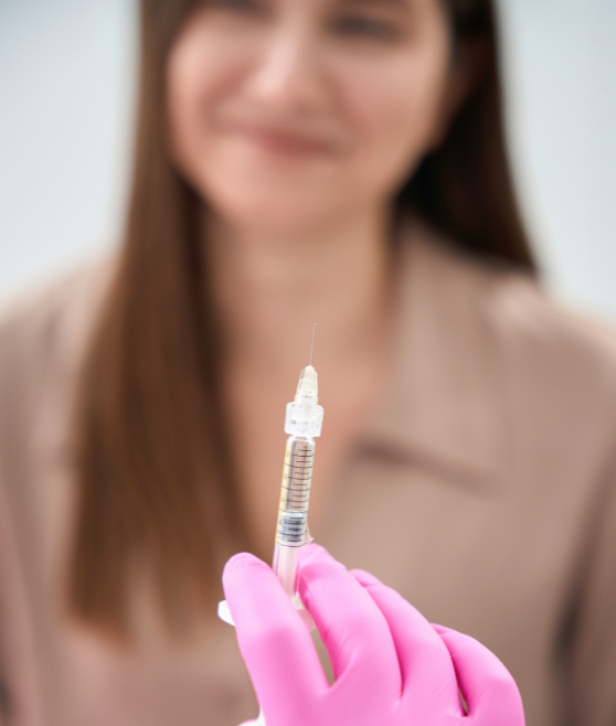 A healthcare worker holding a syringe with a blurred smiling woman in the background.