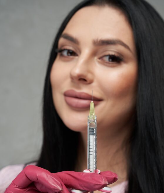 A woman holding a syringe with a needle close to her face.