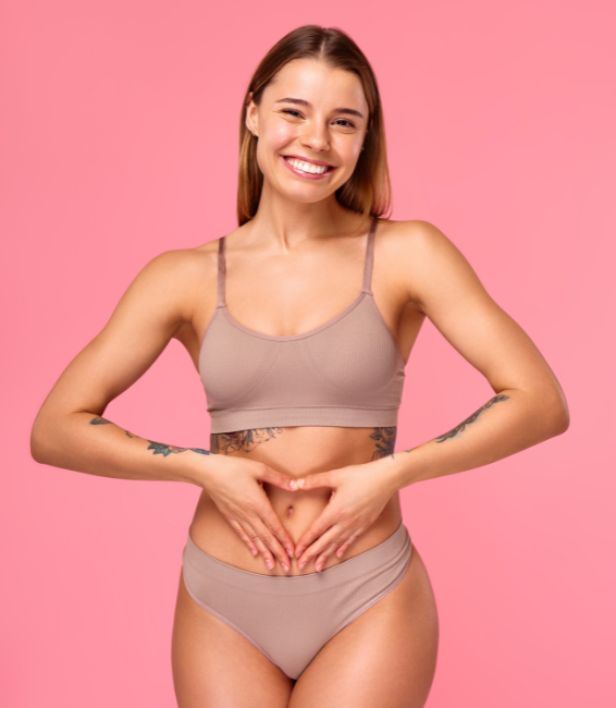 Smiling woman in beige underwear making a heart shape with hands on her stomach.