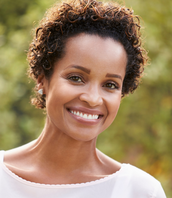 A smiling woman with curly hair outdoors.