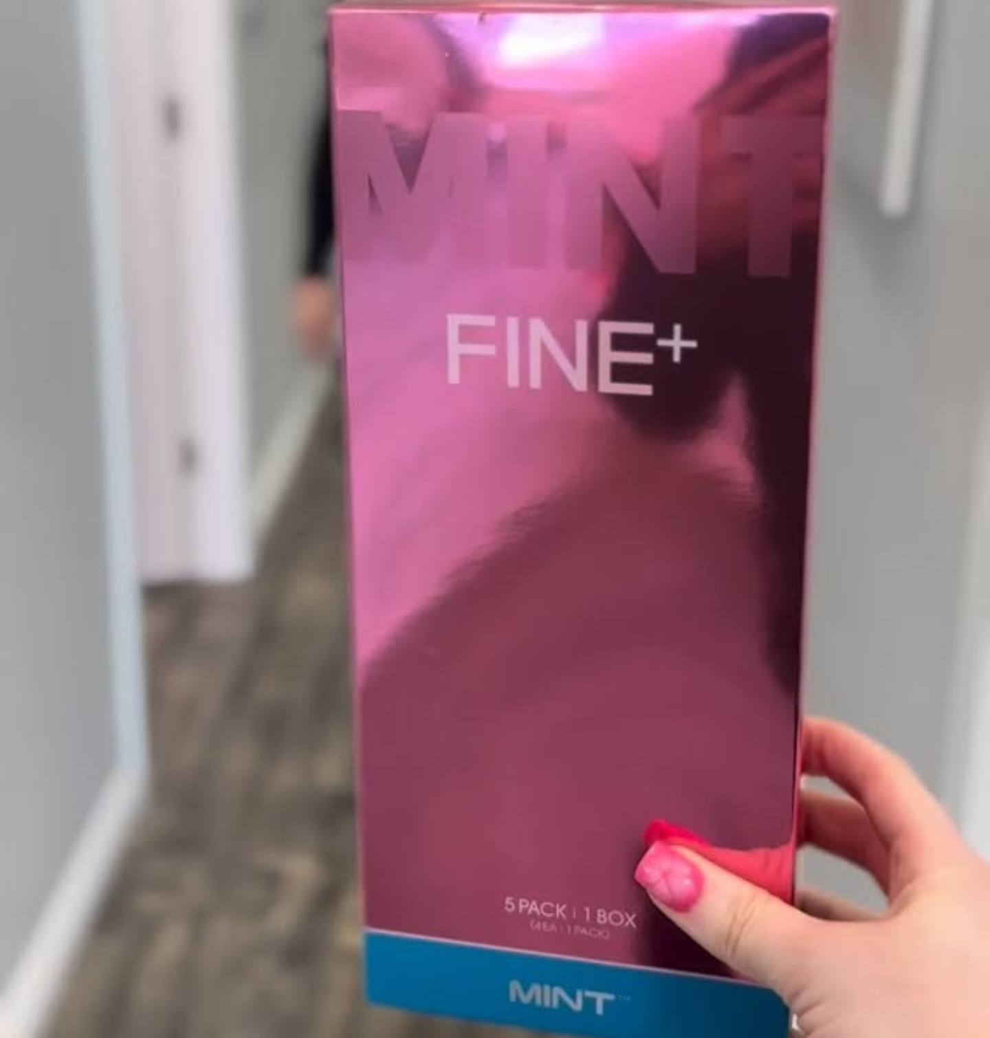 A hand holding a pink box labeled FINE+ MINT in a hallway.