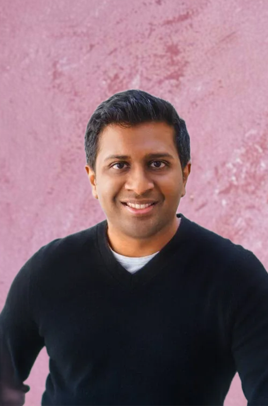 Smiling man in a black shirt against a textured pink wall.