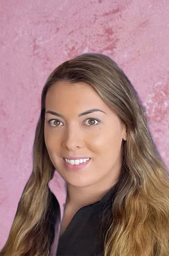 A woman with long light brown hair smiling against a pink background.